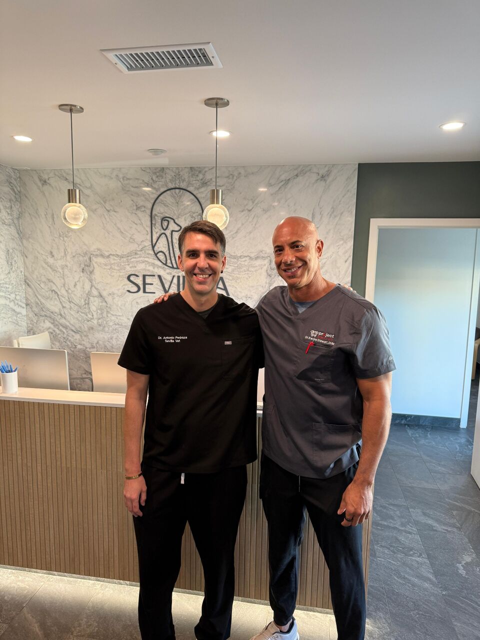 Dr. Pedraza with Dr. Kwane Stewart in front of the Sevilla Vet wall logo